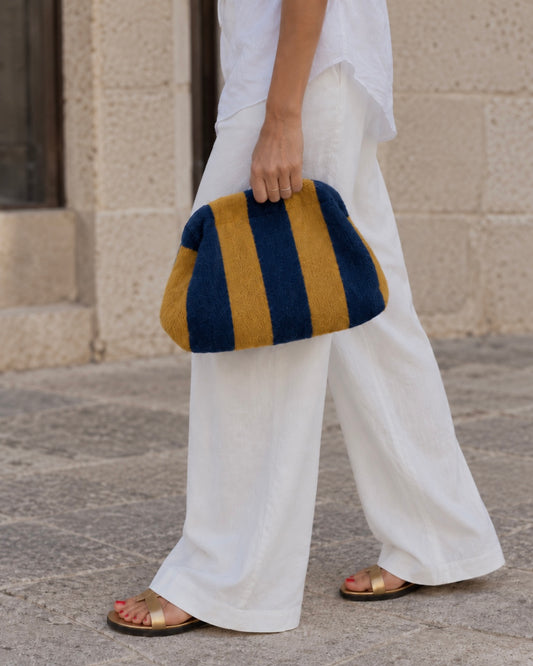 Bolso pouch de rayas azul y mostaza con cadena dorada extraíble, llevado en la mano
