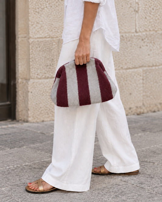 Bolso pouch de rayas burdeos y gris con cadena dorada extraíble, llevado en la mano
