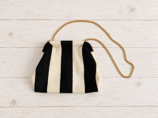 Vista completa del bolso pouch negro y crudo sobre mesa de madera blanca vintage