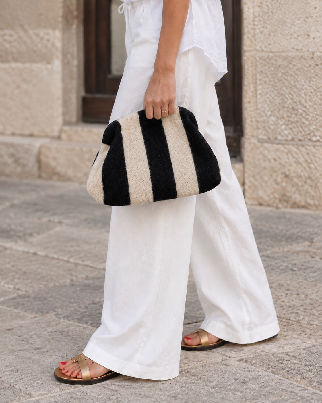 Bolso pouch de rayas negro y crudo con cadena dorada extraíble, llevado en la mano