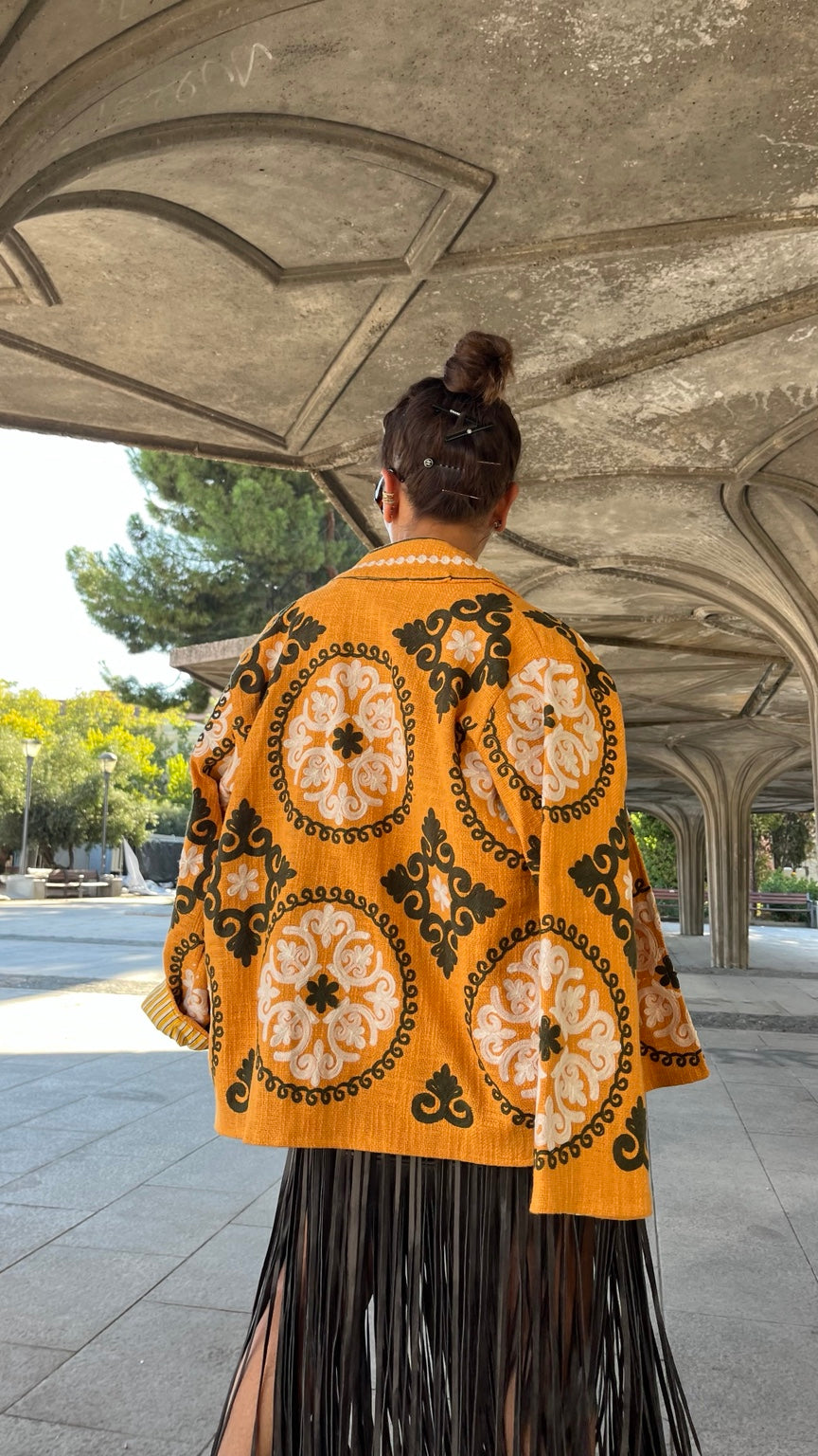 Chaqueta India mostaza bordada - vista de espalda con falda negra de flecos