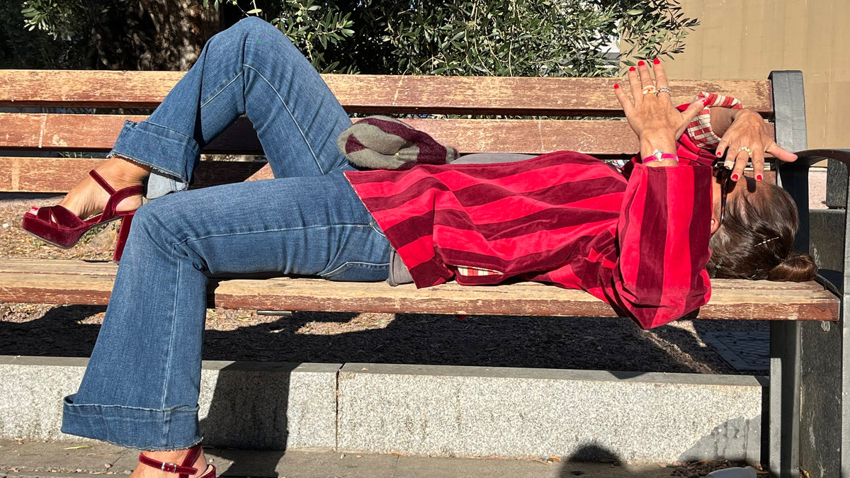 Modelo tumbada en un banco con la chaqueta de terciopelo de rayas rojas.