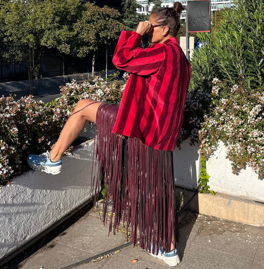 Vista trasera del look con falda berenjena de flecos largos y chaqueta roja.